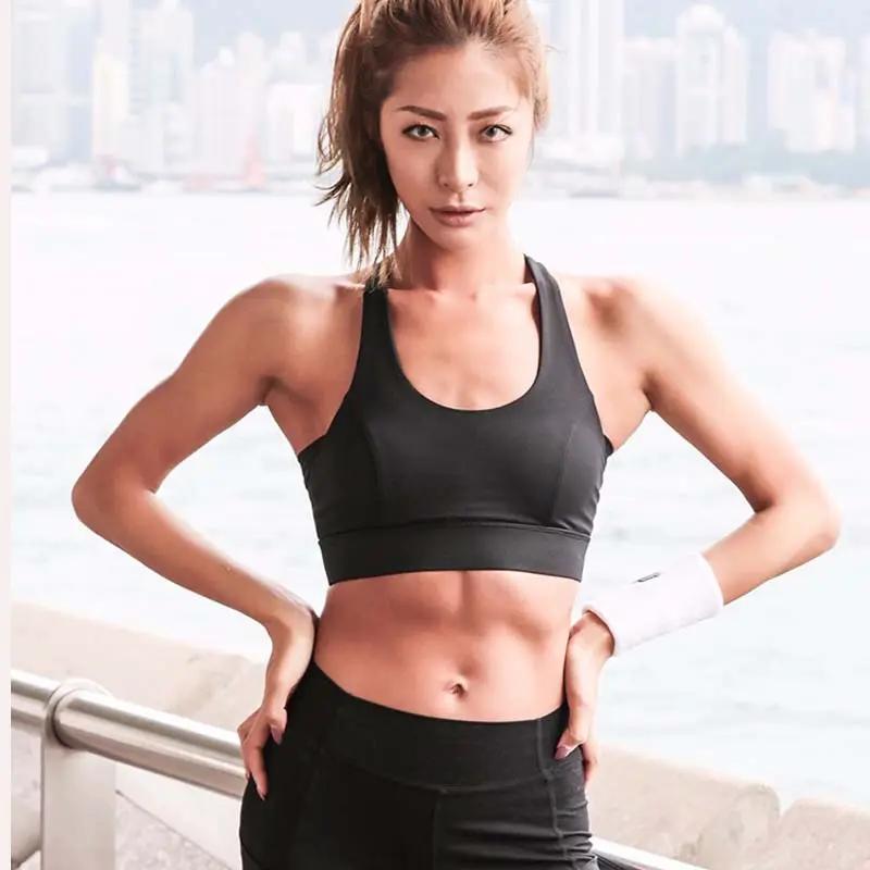 Black push-up sports bra for women with wide straps, athletic top worn by a fit model beside a waterfront cityscape.