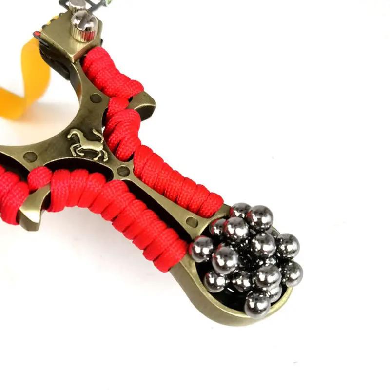 Metal flat-skin slingshot with red paracord wrap and steel BBs in the pouch