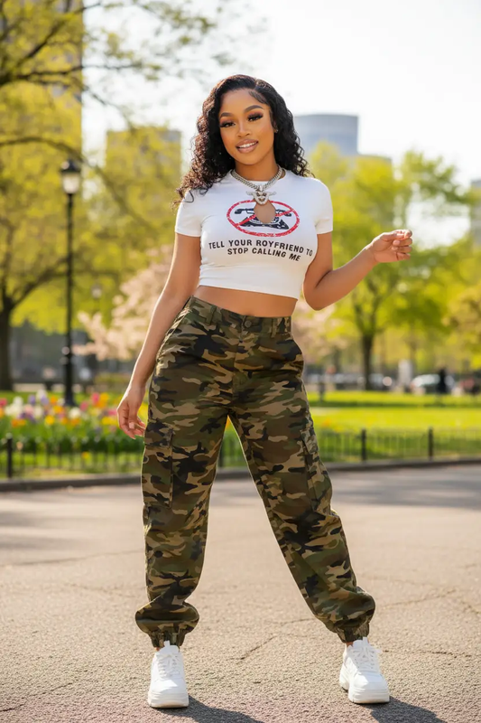 Slogan print white graphic crop top with camouflage cargo pants worn by a woman outdoors